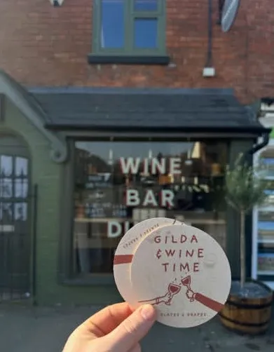 Beer Mat held aloft outside Plates and Grapes